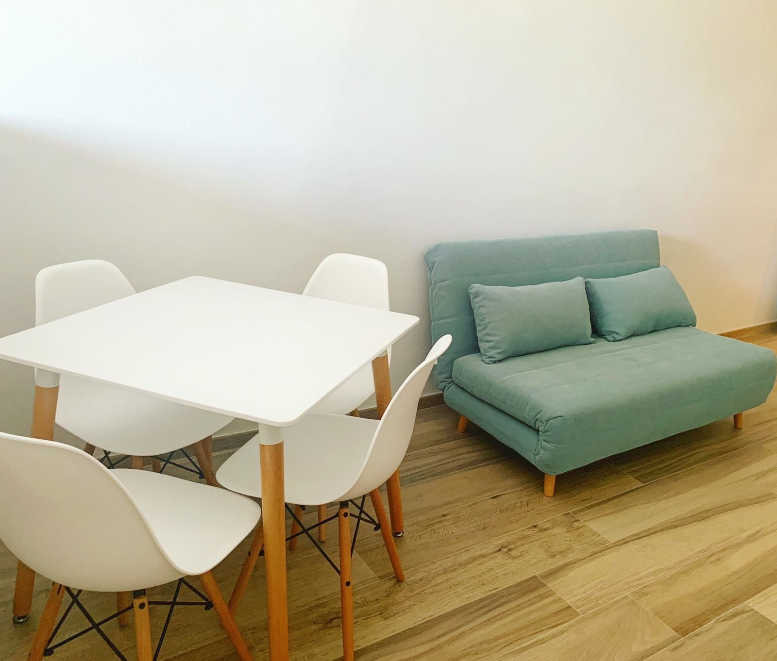 Un coin repas avec une table et des chaises blanches, un canapé de couleur turquoise et un plancher en bois.