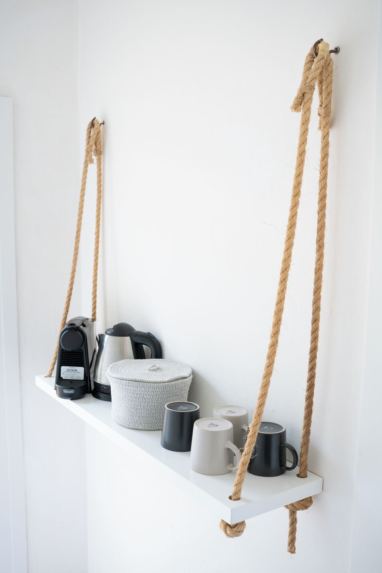 Ein weißes Regal mit Kaffeemaschine, Wasserkochern und Tassen.