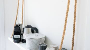 Ein weißes Regal mit Kaffeemaschine, Wasserkochern und Tassen.