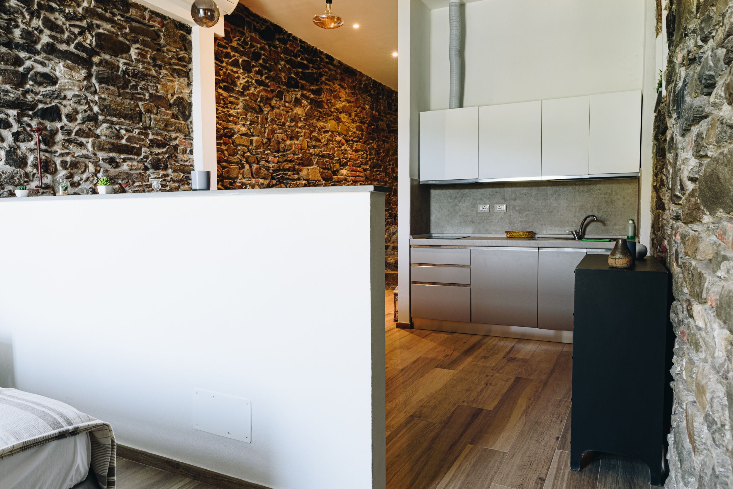 A modern kitchen with stone walls, wooden flooring, and white cabinetry.