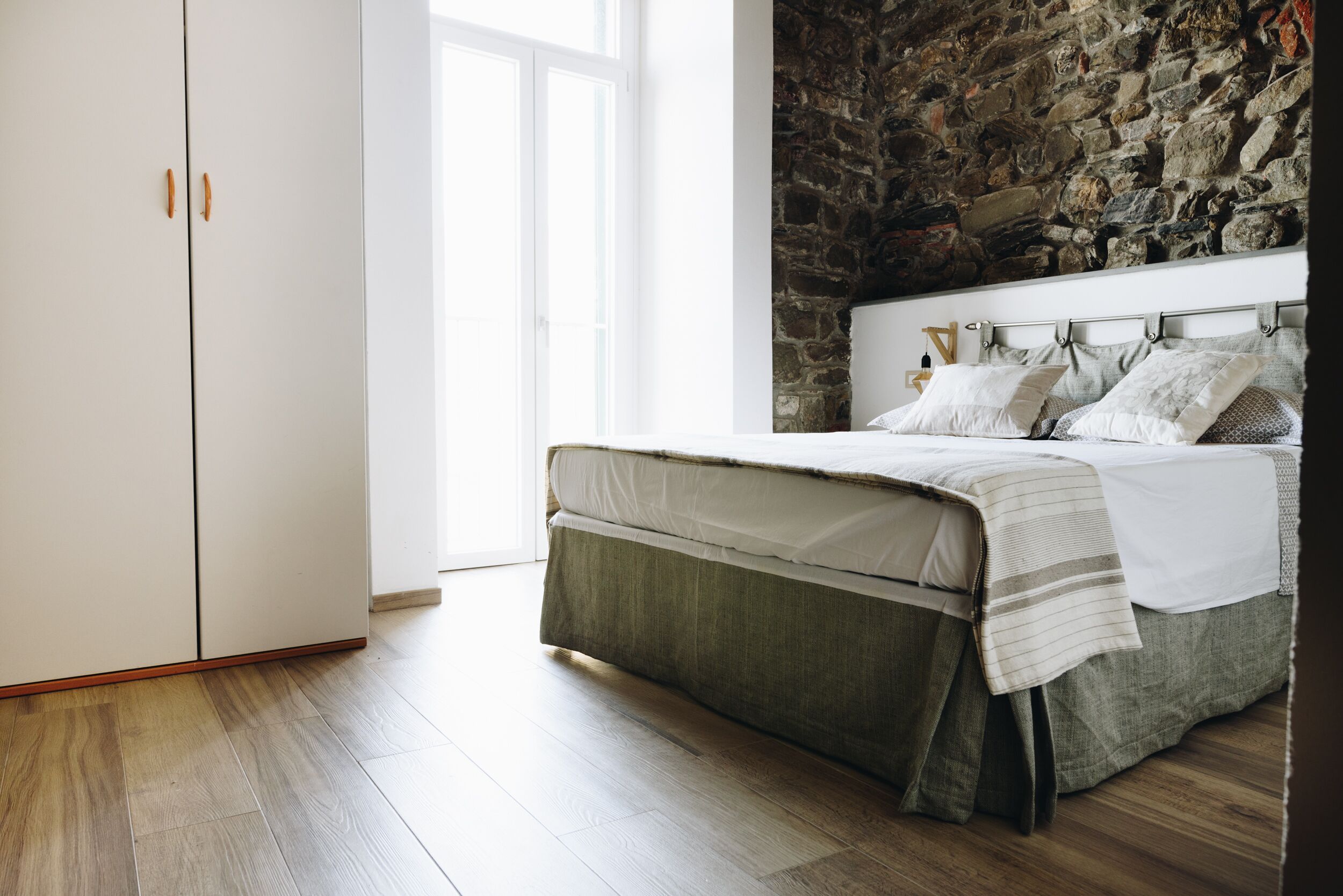 A bedroom with a stone wall, a bed with a headboard, and a wardrobe.