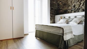 A bedroom with a stone wall, a bed with a headboard, and a wardrobe.