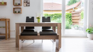 Habitació moderna amb taula de dinar de fusta, cadires negres i vista a un jardí a través d'una finestra gran.