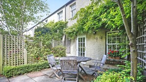 A patio with a round table and four chairs, surrounded by a wooden fence and lush greenery. - Central New Town Apartment (Edinburgh)