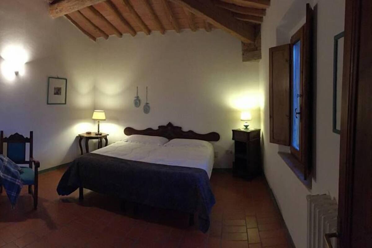 Un dormitorio con una cama, dos mesitas de noche con lámparas, una silla y techo de madera.