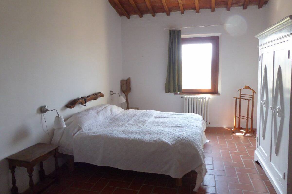 Un dormitorio con cama de madera, una mesita de noche, un radiador, una ventana con cortinas y un armario.