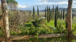 Un paysage rural avec une clôture en bois, de la verdure et des collines à l’horizon.