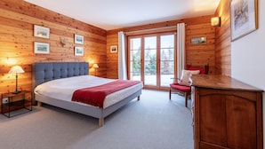 Une chambre avec un grand lit, des murs en bois, une fenêtre et un bureau avec une chaise.