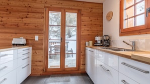 Une cuisine aux murs en bois, avec une grande fenêtre et une vue sur une terrasse extérieure.