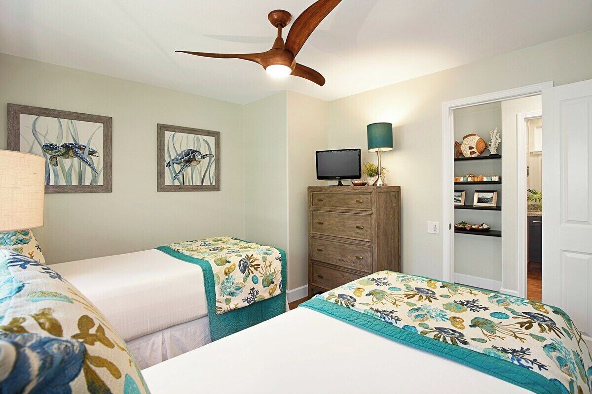 A bedroom with two beds, a ceiling fan, a TV, and a dresser.