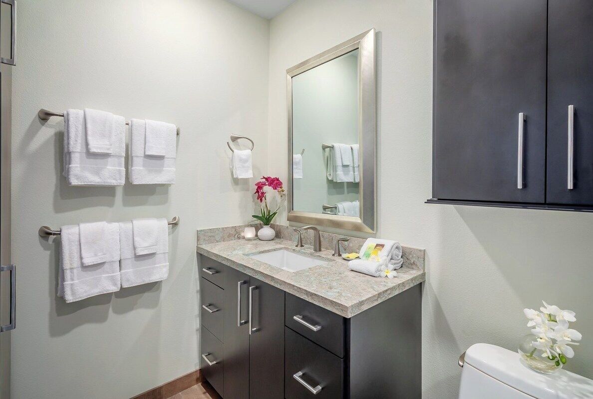 A modern bathroom with a marble sink, dark cabinets, and white towels.