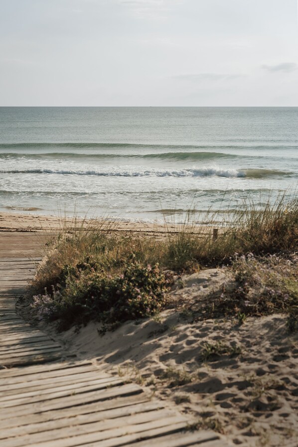 A wooden boardwalk leading to a sandy beach with ocean waves. - Kikopark (Oliva)