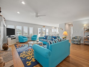 A spacious living room with a large sofa, a television, and a ceiling fan.