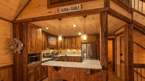 A rustic kitchen with wooden walls, a farmhouse sink, stainless steel appliances, and a bar stool. - Mountain Views | 4 King Bedroom Luxury Cabin | Hot Tub + Fire Pit (Blue Ridge)