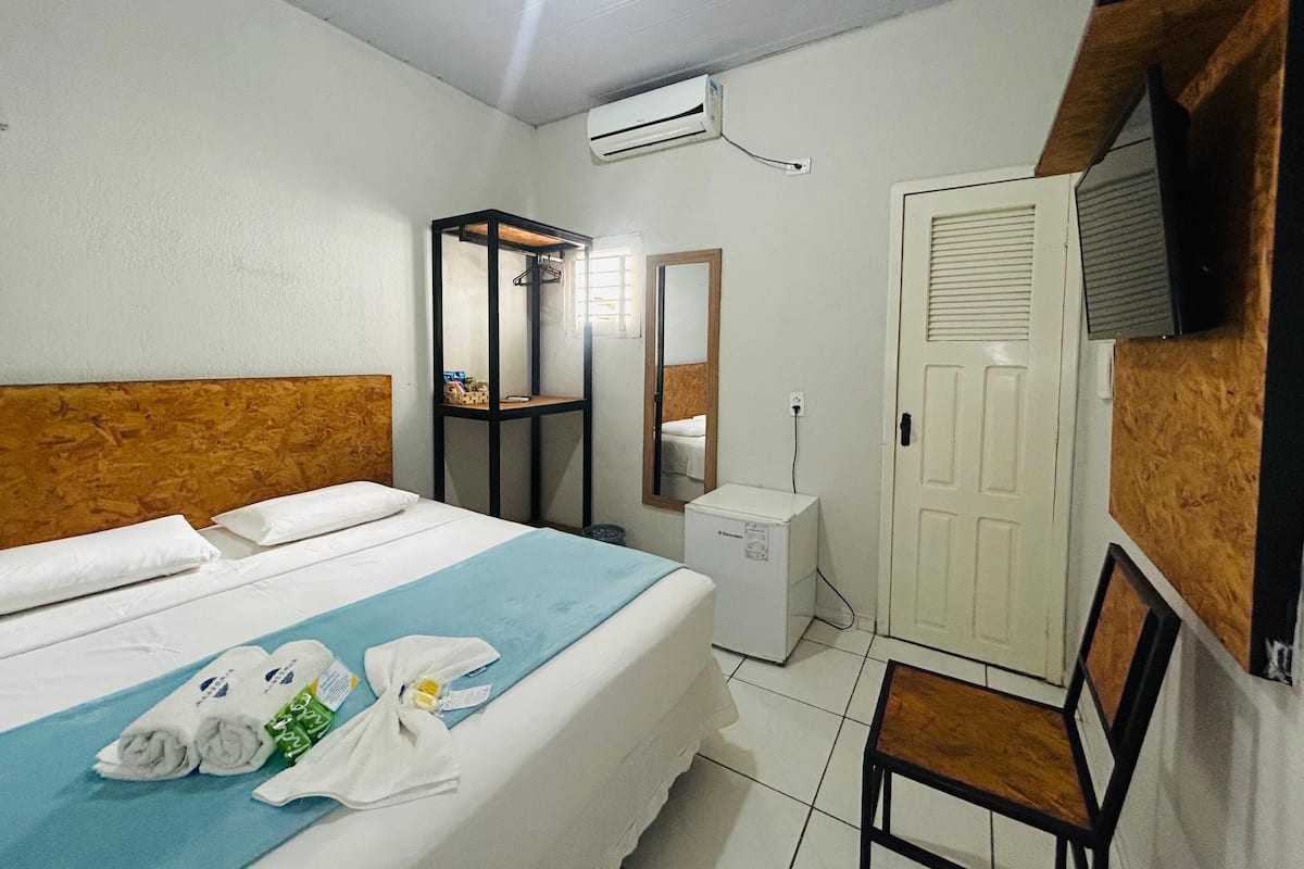 Una habitación de hotel con una cama, un escritorio pequeño, un espejo, aire acondicionado y un armario.