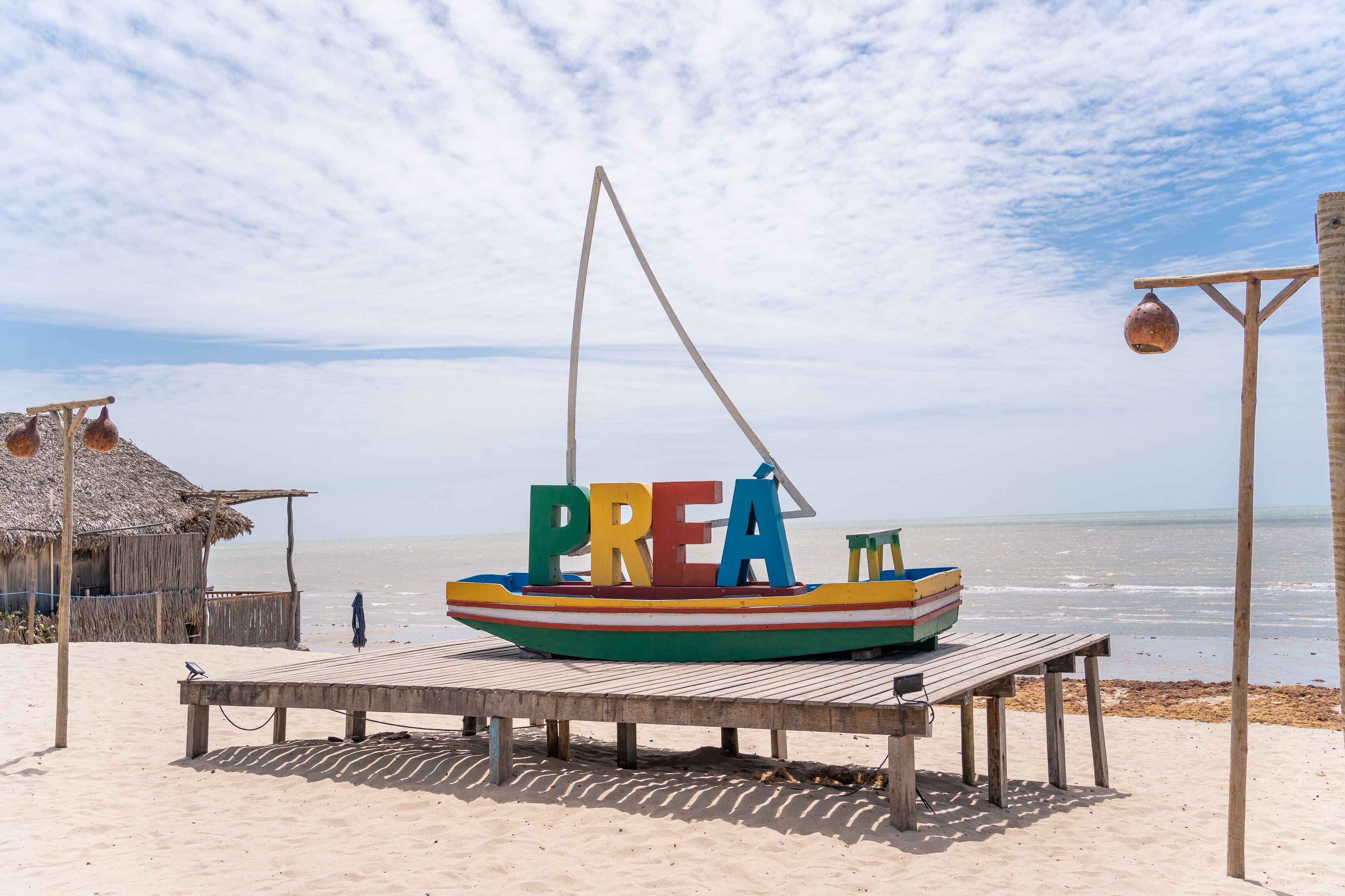 Una embarcación colorida con la palabra 'PREA' en su costado, amarrada a una plataforma de madera en la playa.