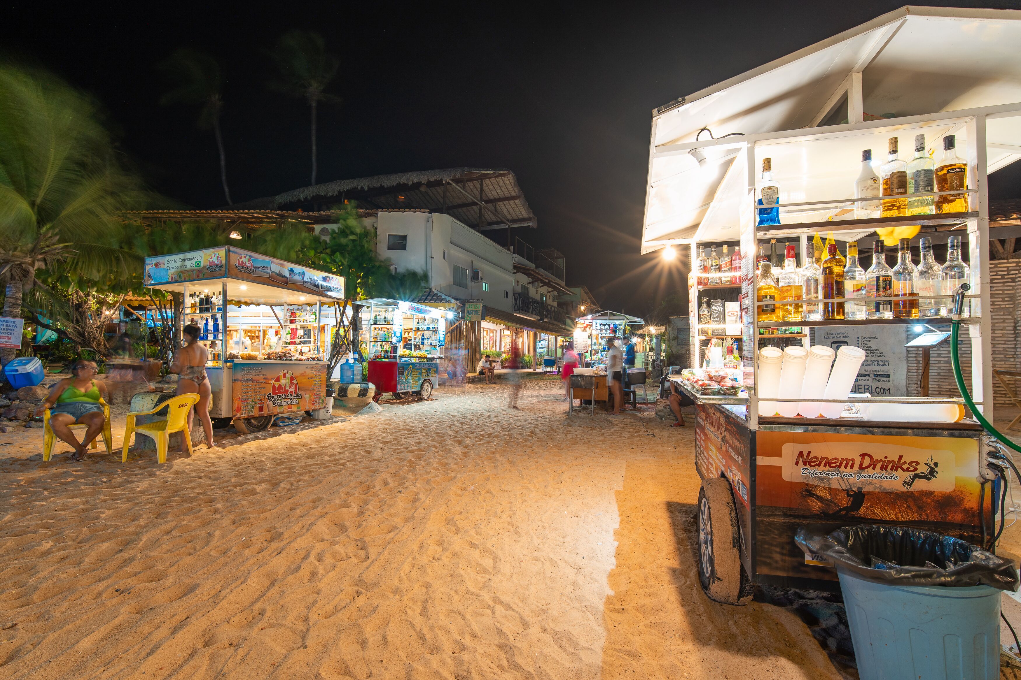 A beachside market with various stalls, including a prominent alcohol kiosk.