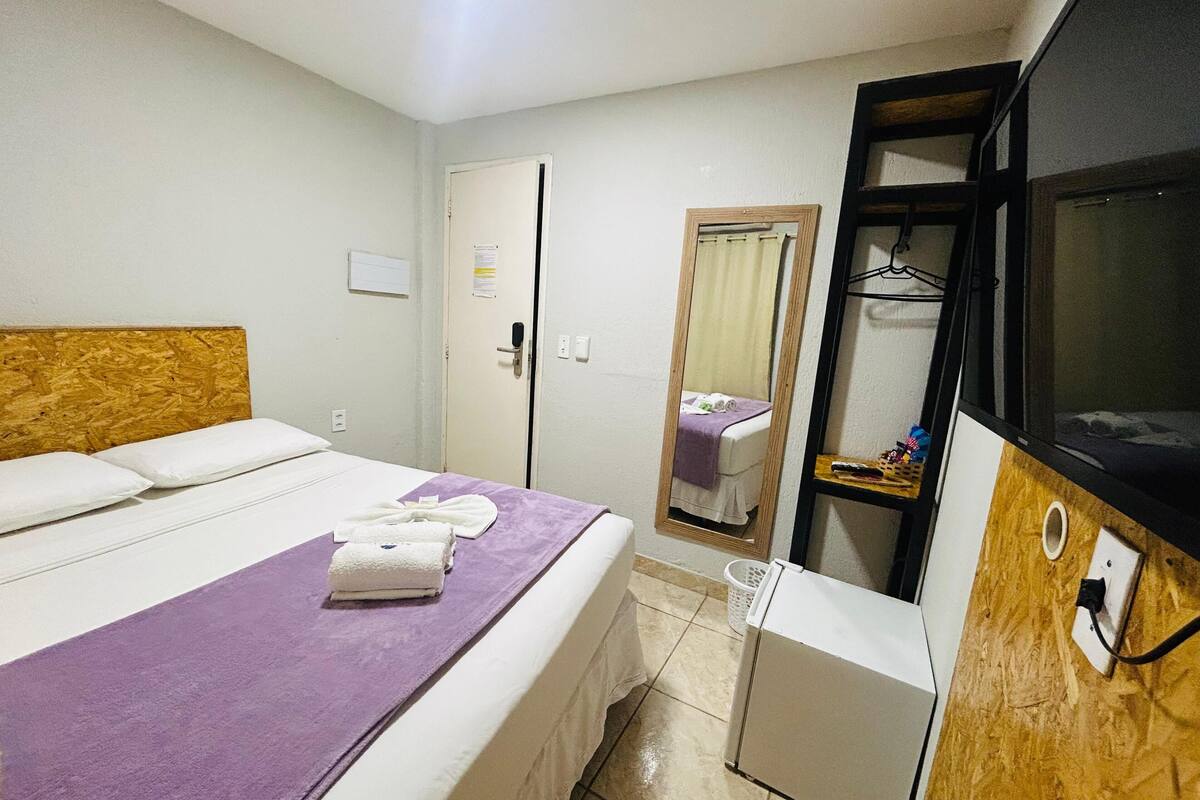 Una habitación de hotel con una cama, un pequeño escritorio, un espejo y una televisión.