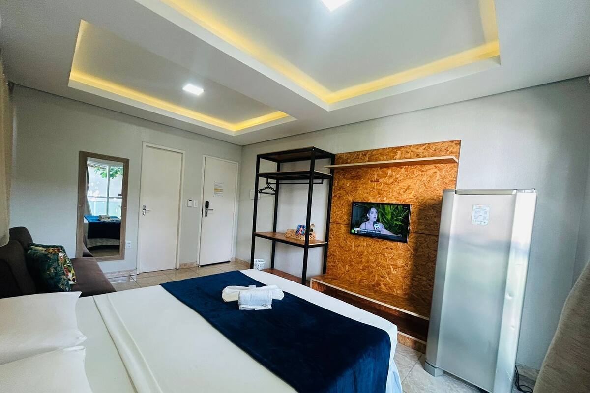 Habitación de hotel con una cama, televisor montado en un panel de madera, refrigerador y armario.