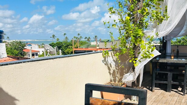Una mesa con diferentes opciones de desayuno, como sándwiches, una taza de café y un vaso de jugo, ubicada en una terraza con vista al mar y edificios al fondo.