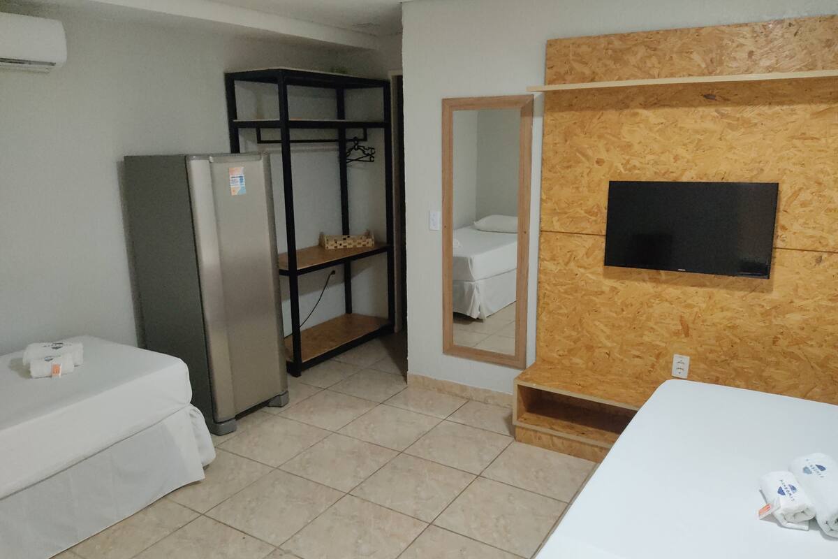 Una habitación pequeña y limpia con una cama, un refrigerador, un estante de madera y un televisor fijado a un panel de madera.