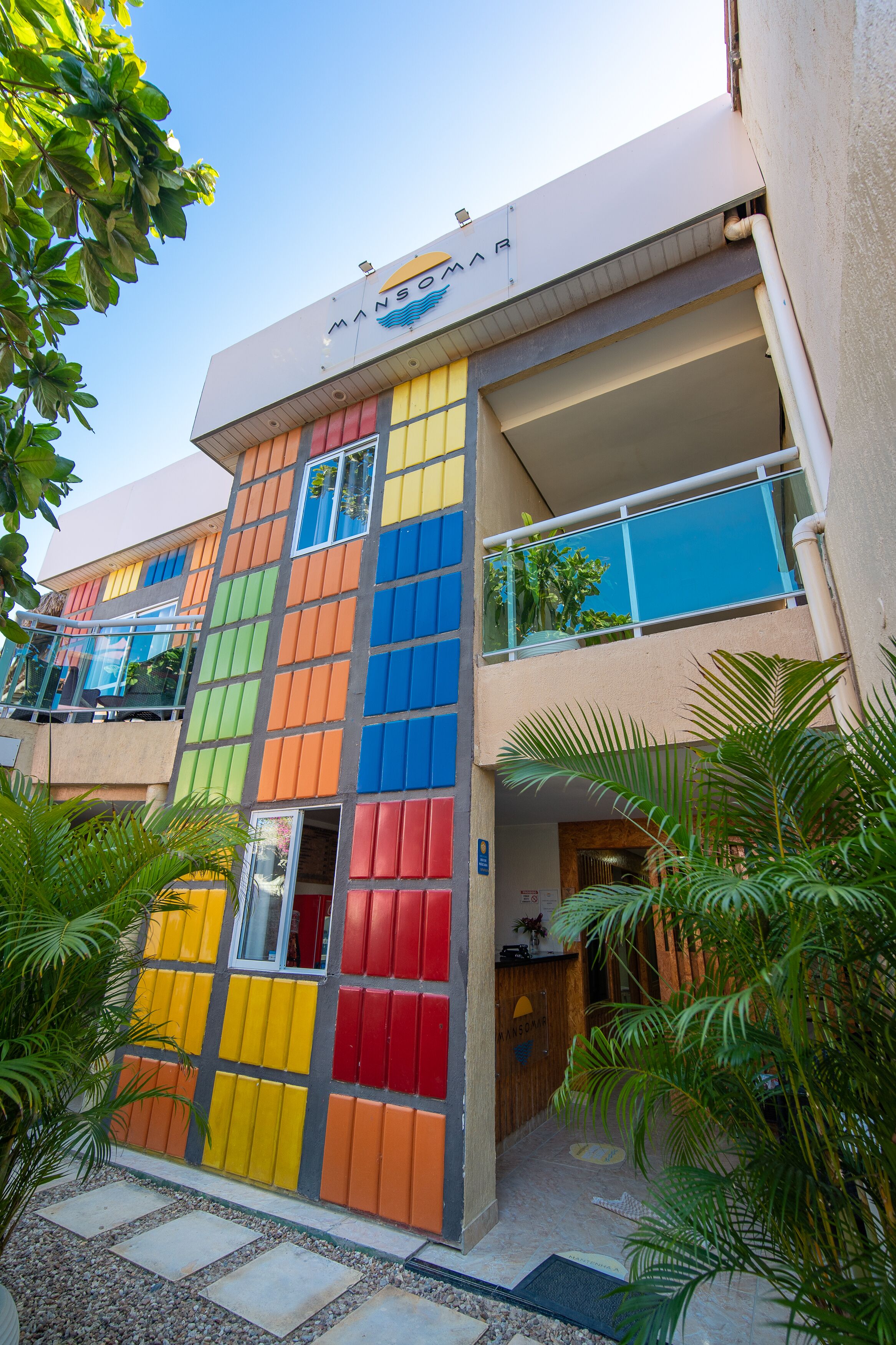 Un edificio de varios pisos con fachada colorida, una entrada visible y un balcón con barandas de vidrio.