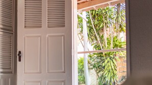 Una puerta blanca con ventana, que da a un espacio exterior cubierto con vista a un árbol y un muro de ladrillo.