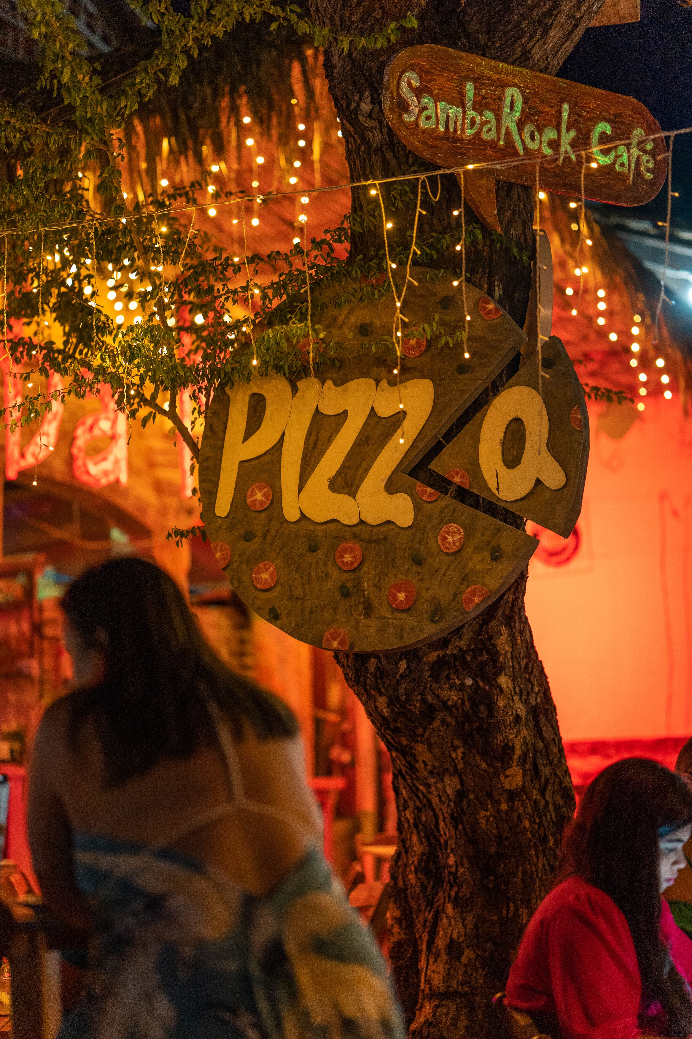 A tree with a sign that reads "Samba Rock Cafe" and another sign that says "Pizza."