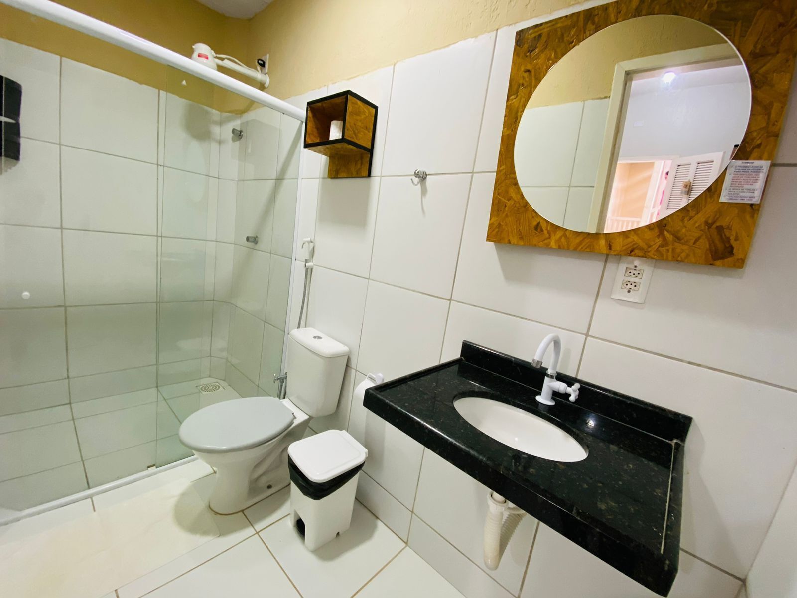 Ein Badezimmer mit einer Duschkabine, einer Toilette, einem Waschbecken mit schwarzer Arbeitsplatte und einem Spiegel mit Holzrahmen.
