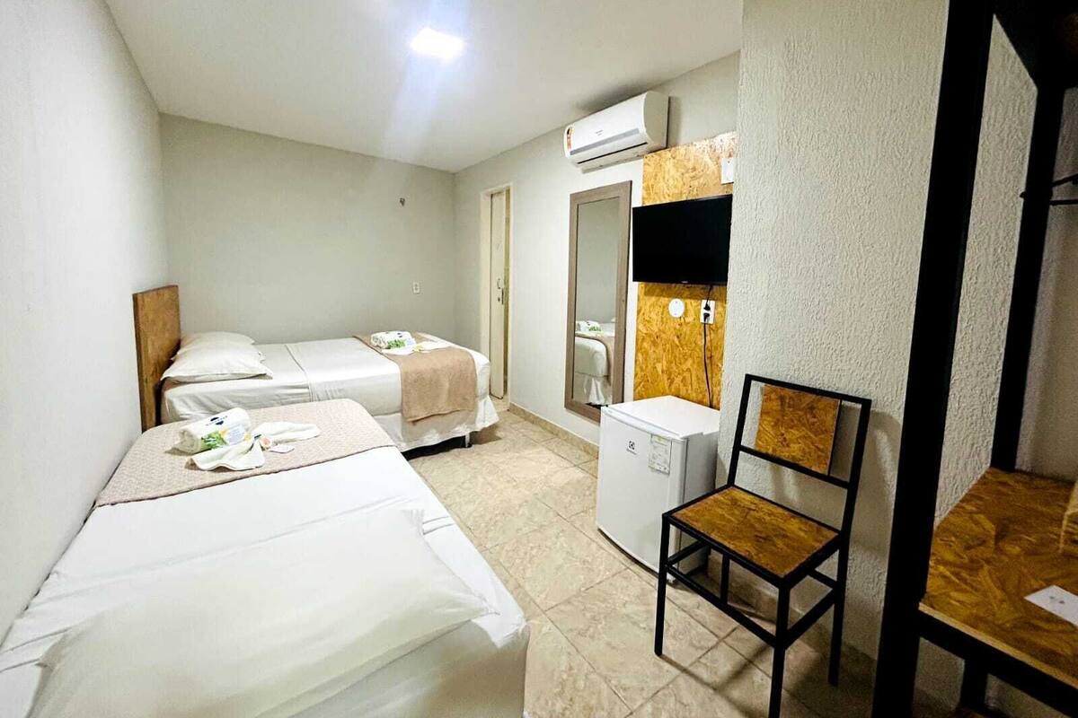 Una habitación de hotel con dos camas, un escritorio, una silla, un espejo y un televisor.