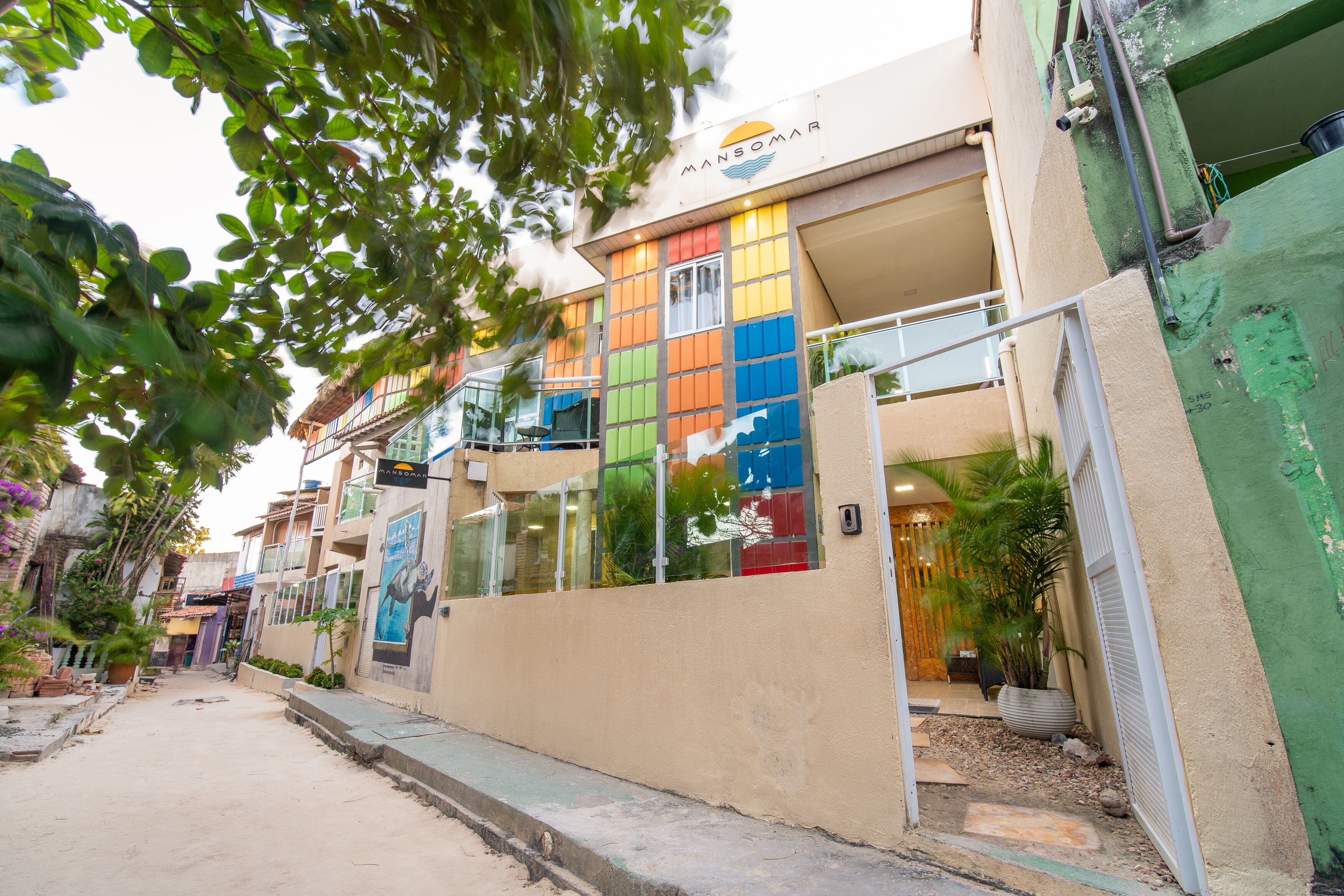Un edificio con fachada colorida, una entrada visible y un pequeño jardín con plantas.