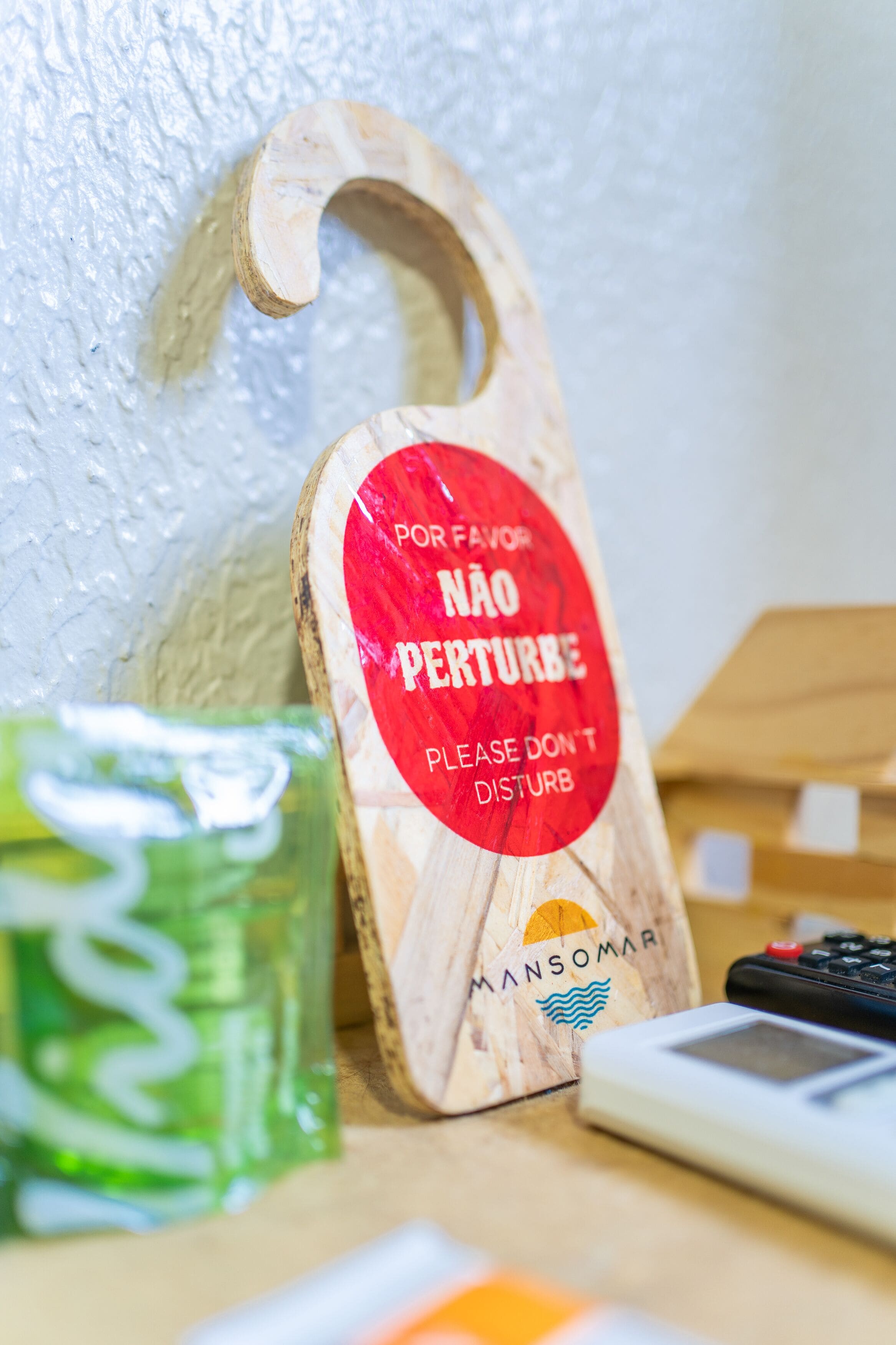 Un letrero de madera con un círculo rojo y texto en portugués, una botella verde y una calculadora sobre una mesa.