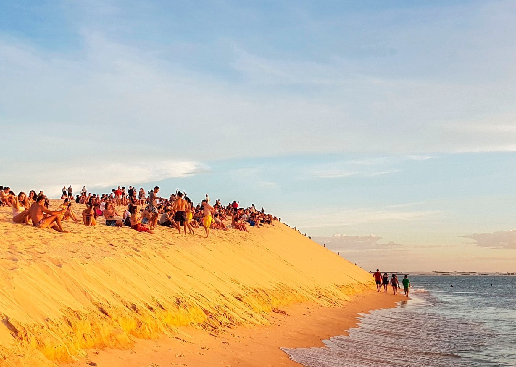 A crowded beach with people sitting and walking along the sand.