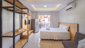 Una habitación de hotel con cama, sofá, estantería de madera y ventana con cortinas.