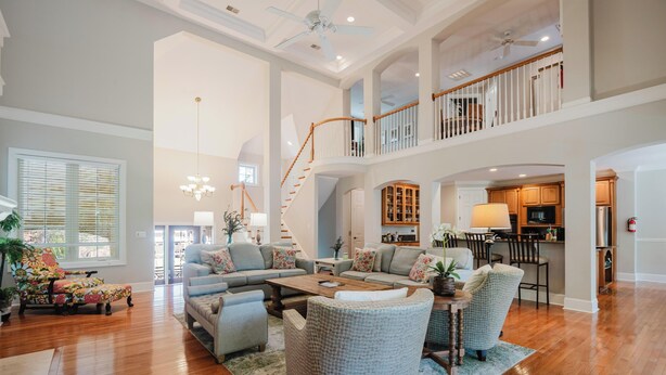 A spacious living area with a high ceiling, a staircase leading to an upper level, and a kitchen visible in the background. - 28 Moonshell - Luxury in Folly Field (Hilton Head Island)