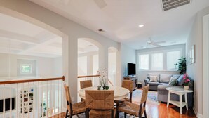 A spacious living area with a dining table, wicker chairs, a sofa, a TV, and a ceiling fan. - 28 Moonshell - Luxury in Folly Field (Hilton Head Island)