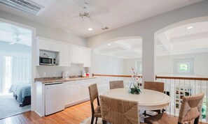 A modern kitchen with white cabinets, a microwave, and a coffee maker. There is a dining area with a round table and wicker chairs. - 28 Moonshell - Luxury in Folly Field (Hilton Head Island)