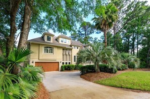 A two-story house with a garage, surrounded by trees and a well-maintained lawn. - 28 Moonshell - Luxury in Folly Field (Hilton Head Island)