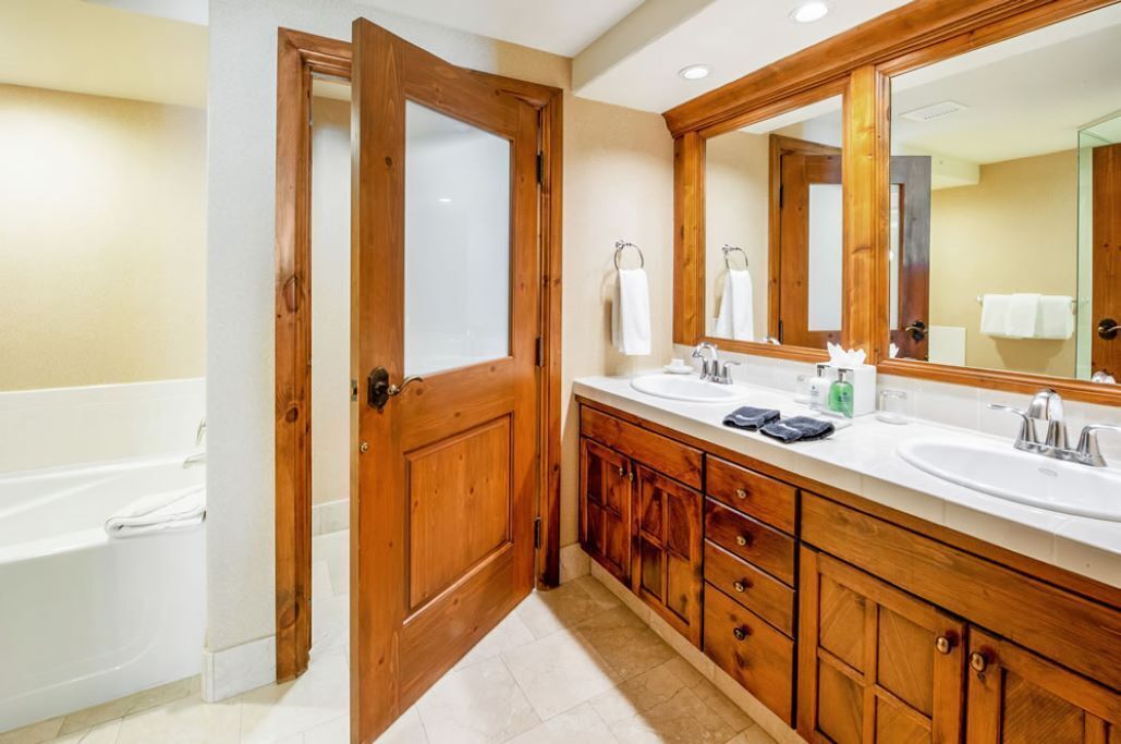 A bathroom with wooden cabinetry, two sinks, a large mirror, and a bathtub.