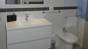 A bathroom with a large sink, a mirror, a bidet, and a trash bin. - B&B Fradama' Holiday Dorgali (Dorgali)