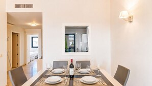 Een eethoek met een tafel gedekt voor vier personen, een wijnfles en uitzicht op de keuken door een raam.