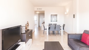 Een moderne woonkamer met een flatscreen televisie, een bank en een eethoek met een tafel en stoelen.