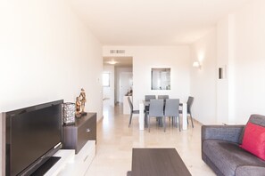 A modern living room with a flat-screen TV, a sofa, and a dining area with a table and chairs.