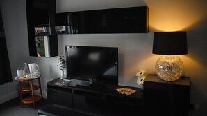 A modern hotel room with a flat-screen TV, a small table with a lamp, and a chair. - TLC Exmouth Bed and Breakfast (Exmouth)