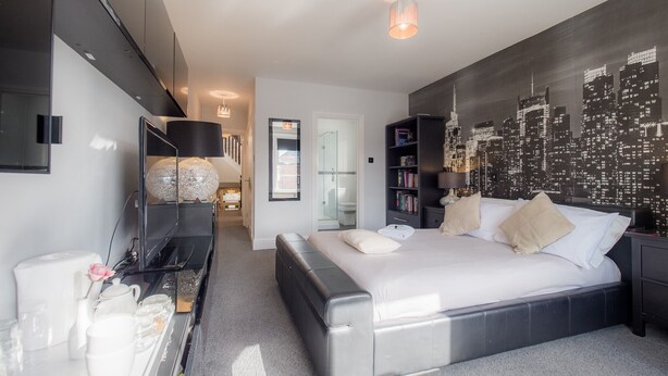 A modern bedroom with a cityscape mural, a large bed, a desk with a lamp, and a bookshelf. - TLC Exmouth Bed and Breakfast (Exmouth)