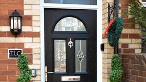 A black front door with a glass panel and a decorative metal piece above it. There are two potted plants on either side of the door, and a 'WELCOME' sign on the ground. - TLC Exmouth Bed and Breakfast (Exmouth)