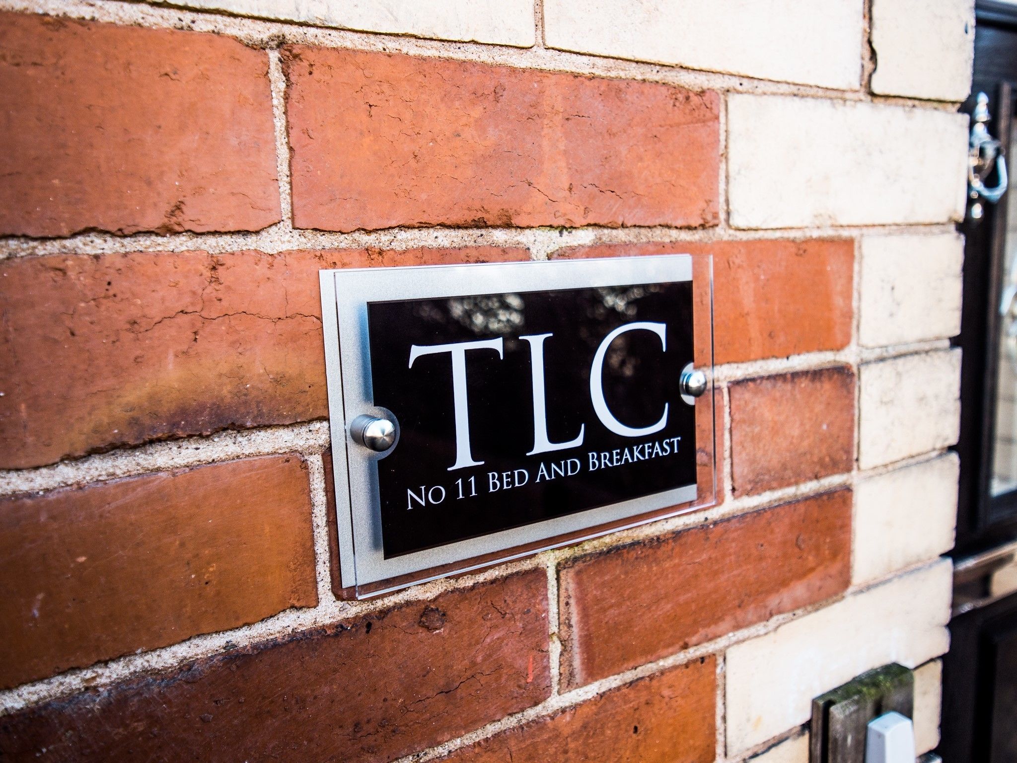 A black sign with white lettering on a brick wall, indicating "TLC No 11 Bed and Breakfast".