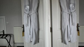 A room with a white door, two white robes hanging on the door, a radiator, and a black chair. - TLC Exmouth Bed and Breakfast (Exmouth)