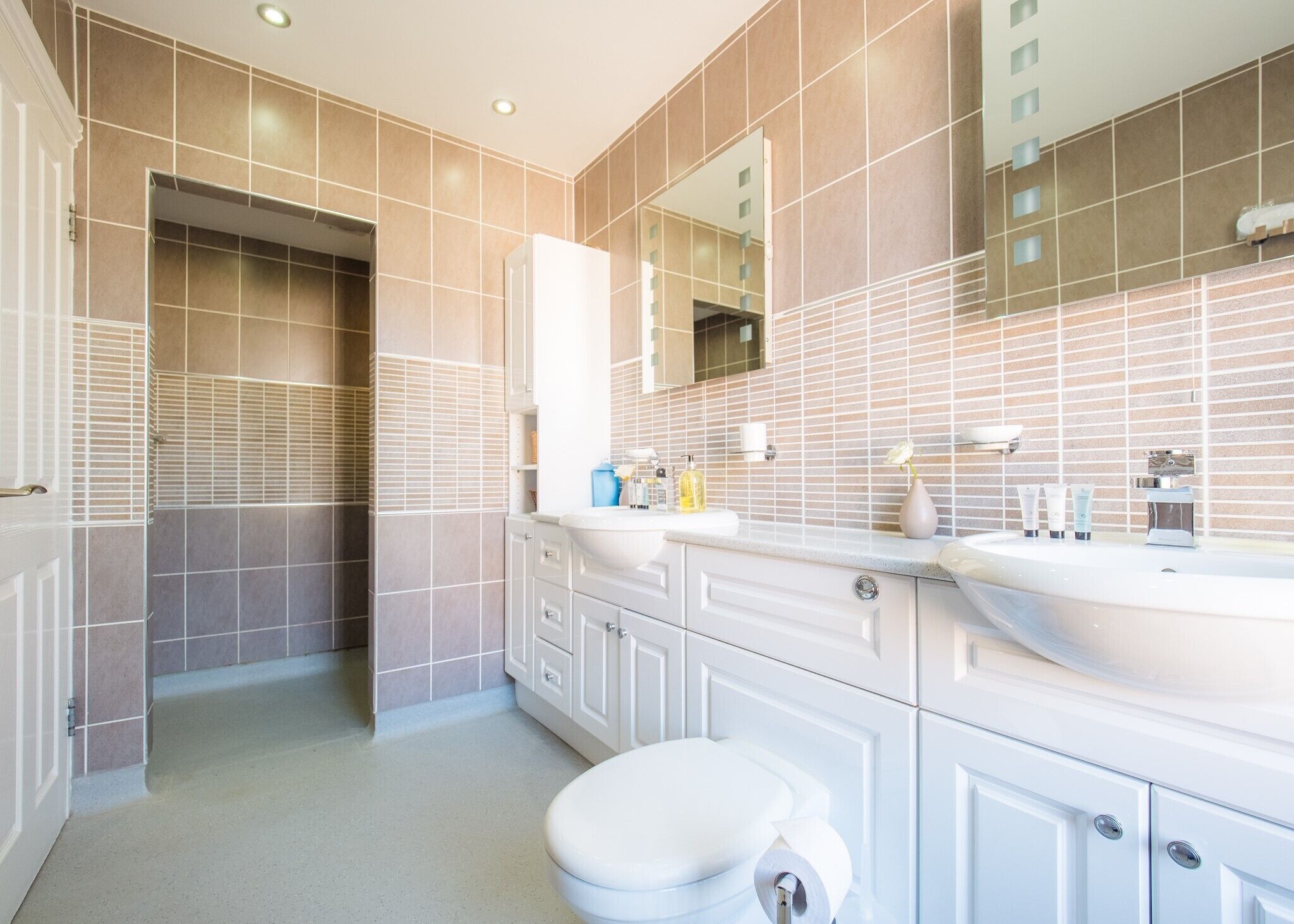 A modern bathroom with a large mirror, two sinks, and a toilet.