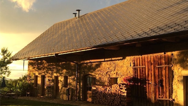 Un bâtiment rustique en pierre, doté d’un toit en pente, de portes en bois et d’une pile de bois de chauffage devant l’entrée.